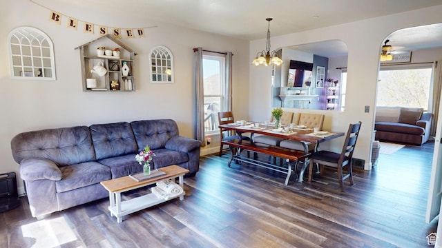 living area featuring wood finished floors, a chandelier, ceiling fan, arched walkways, and baseboards
