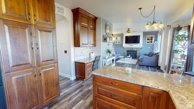 kitchen featuring a glass covered fireplace, dark wood-style flooring, ceiling fan, light stone countertops, and a chandelier