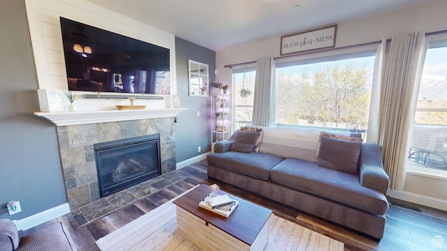 living area with plenty of natural light, wood finished floors, a tile fireplace, and baseboards