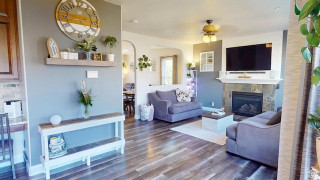 living room with a ceiling fan, a tiled fireplace, wood finished floors, and arched walkways