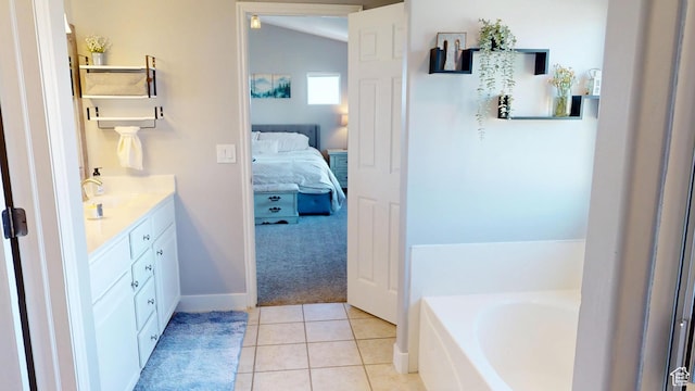 ensuite bathroom featuring a bath, vanity, tile patterned flooring, vaulted ceiling, and baseboards