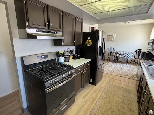 527 W Palisade Dr, Moab, UT 84532 - kitchen with stainless steel gas stove, under cabinet range hood, light wood-style floors, black fridge, and dark brown cabinetry