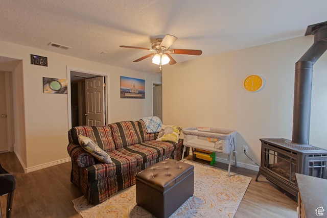 living area with a wood stove, wood finished floors, a ceiling fan, and baseboards