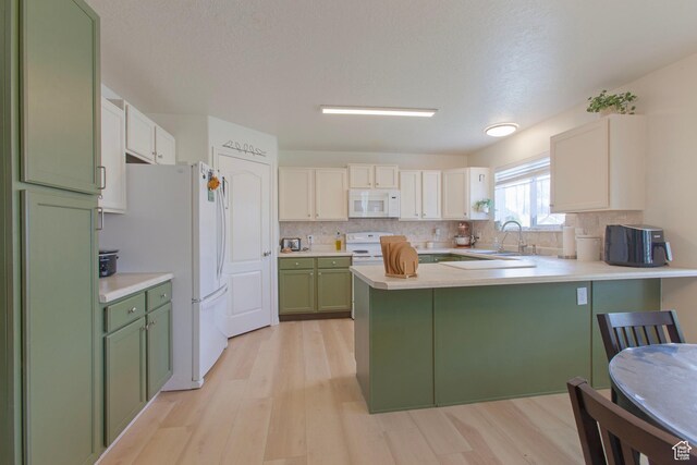 kitchen with green cabinets, white appliances, a peninsula, a sink, and light countertops
