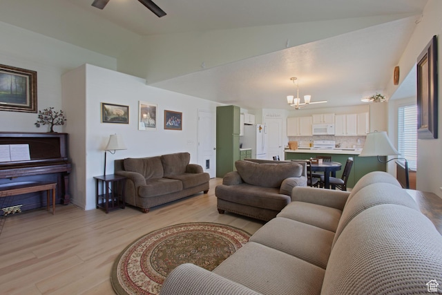living area featuring a chandelier, light wood finished floors, ceiling fan, and high vaulted ceiling