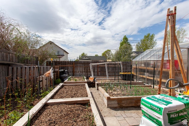 view of playground featuring a greenhouse, a vegetable garden, a fenced backyard, and an outdoor structure