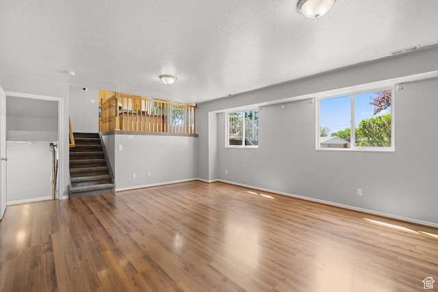 unfurnished living room with stairway, wood finished floors, baseboards, and a textured ceiling