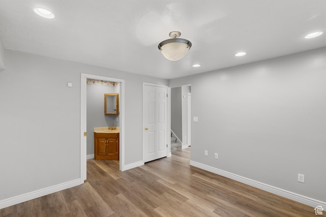 unfurnished bedroom featuring wood finished floors, baseboards, recessed lighting, a sink, and ensuite bath