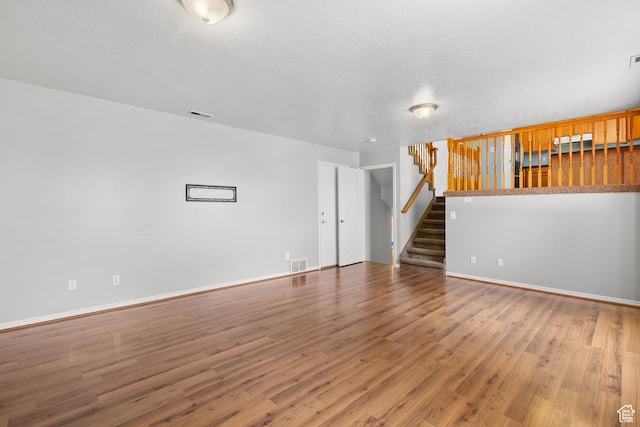 unfurnished living room featuring wood finished floors, stairway, and baseboards