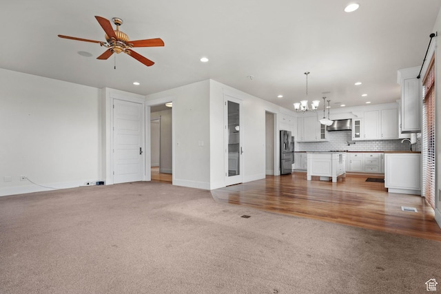 unfurnished living room with recessed lighting, light colored carpet, ceiling fan, a chandelier, and baseboards
