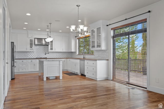 kitchen featuring wall chimney range hood, stainless steel appliances, backsplash, a chandelier, and white cabinets