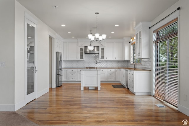 kitchen featuring appliances with stainless steel finishes, a chandelier, wall chimney exhaust hood, backsplash, and recessed lighting