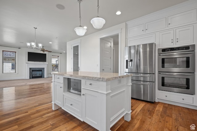 kitchen with stainless steel appliances, white cabinets, decorative light fixtures, a glass covered fireplace, and a chandelier