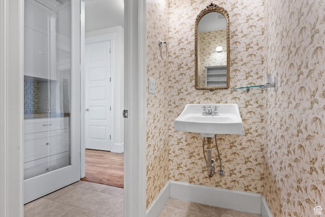 bathroom featuring tile patterned floors, baseboards, wallpapered walls, and a sink