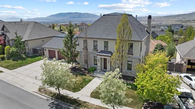 view of front facade with stone siding, stucco siding, a residential view, an attached garage, and a mountain view