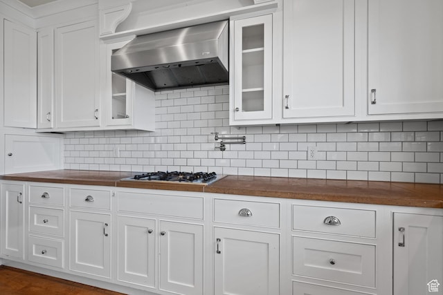 kitchen featuring wall chimney exhaust hood, gas cooktop, wood counters, white cabinetry, and glass insert cabinets