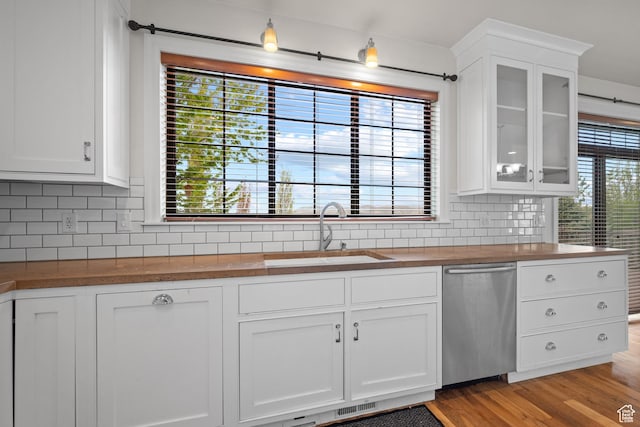 kitchen with wooden counters, stainless steel dishwasher, a sink, and tasteful backsplash