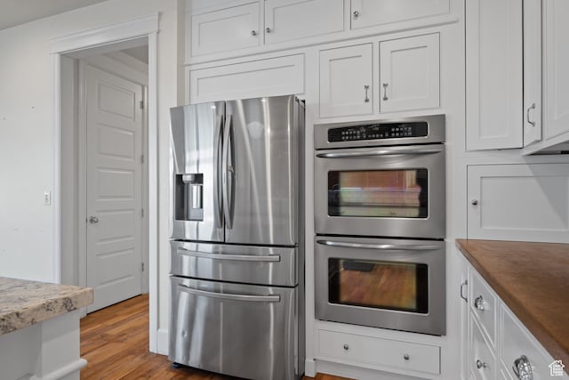 kitchen with appliances with stainless steel finishes, white cabinets, and wood finished floors