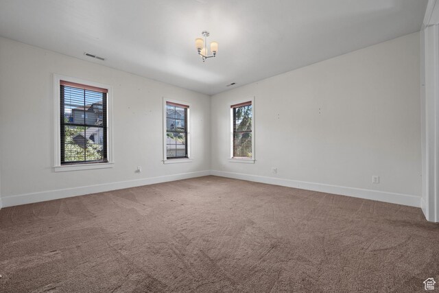 carpeted empty room featuring baseboards, plenty of natural light, and a chandelier