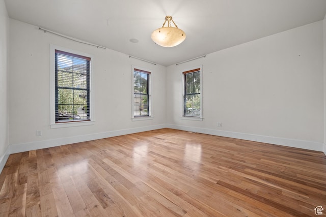 empty room featuring light wood finished floors, plenty of natural light, and baseboards