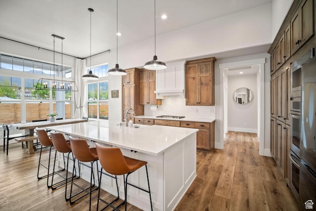 kitchen with light countertops, decorative backsplash, stainless steel appliances, a large island, and a sink