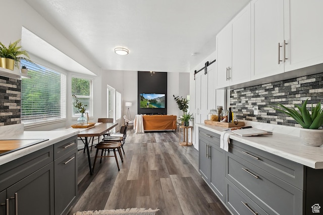 kitchen with dark wood finished floors, backsplash, light countertops, a barn door, and gray cabinetry