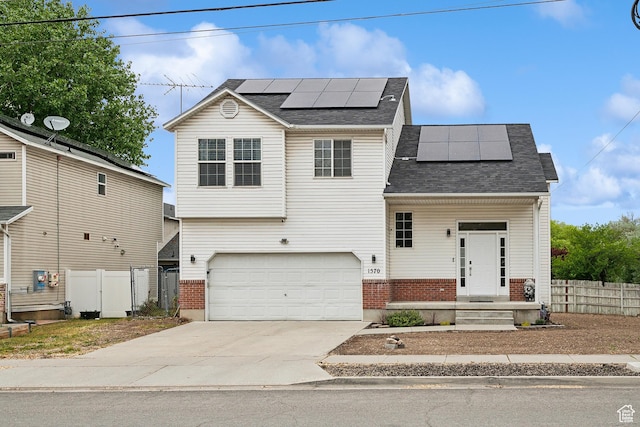 traditional home with brick siding, roof mounted solar panels, concrete driveway, fence, and an attached garage