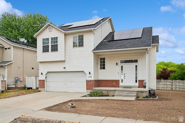view of front of property featuring roof mounted solar panels, fence, an attached garage, concrete driveway, and a shingled roof