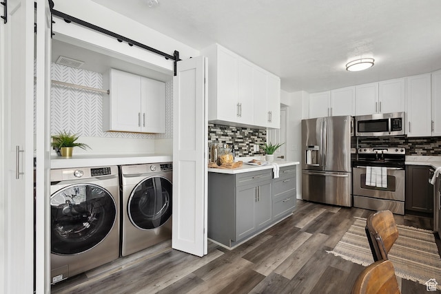 laundry room featuring independent washer and dryer, dark wood-style flooring, and a barn door