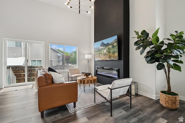 living room with wood finished floors, a towering ceiling, a glass covered fireplace, baseboards, and a chandelier
