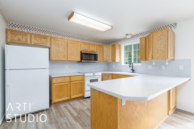 kitchen with white appliances, light wood-style flooring, light countertops, a peninsula, and a sink