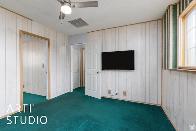 unfurnished bedroom featuring wooden walls, carpet flooring, multiple windows, and ceiling fan