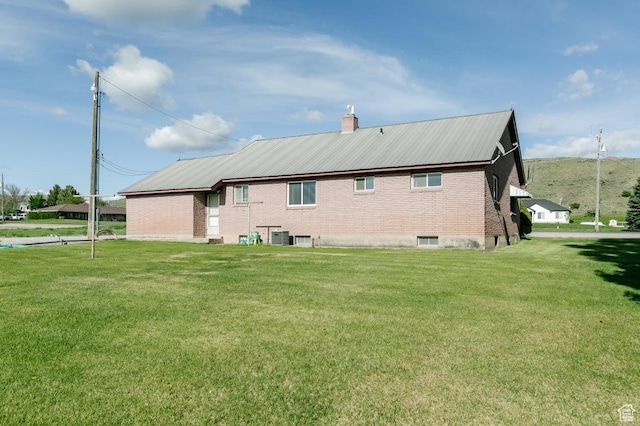 back of property featuring a lawn, brick siding, and a chimney
