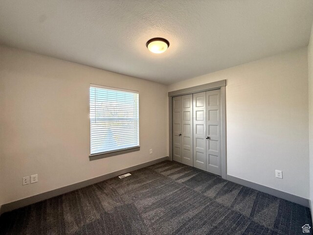 unfurnished bedroom featuring baseboards, dark carpet, a closet, and a textured ceiling