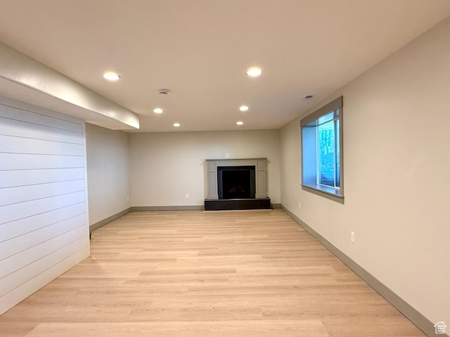unfurnished living room featuring recessed lighting, a tiled fireplace, light wood-style flooring, and baseboards