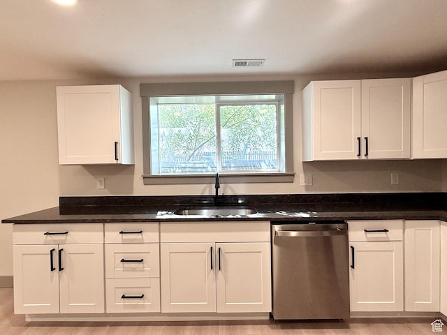 kitchen featuring stainless steel dishwasher, white cabinetry, a sink, and light wood finished floors