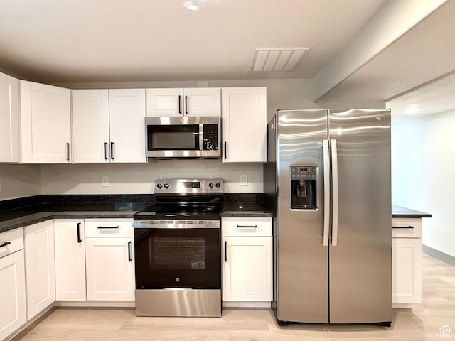 kitchen featuring stainless steel appliances, dark countertops, light wood-style floors, and white cabinetry