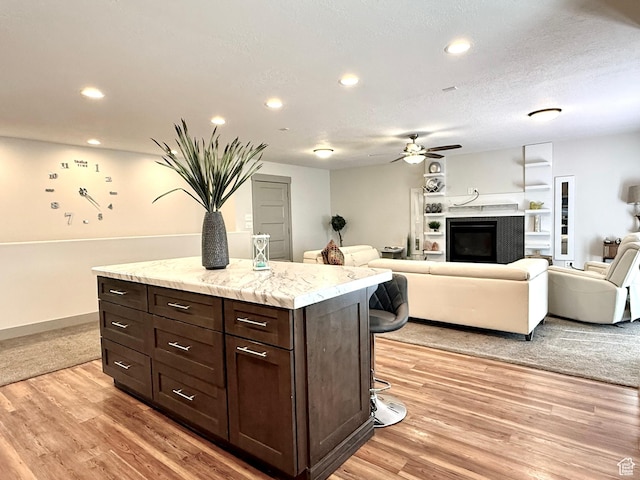 kitchen featuring ceiling fan, light wood-style flooring, dark brown cabinetry, a breakfast bar area, and recessed lighting