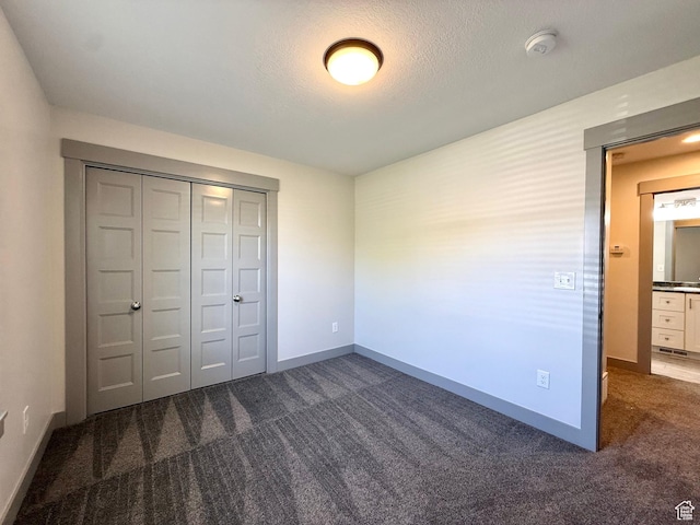 unfurnished bedroom with dark colored carpet, baseboards, a closet, and a textured ceiling