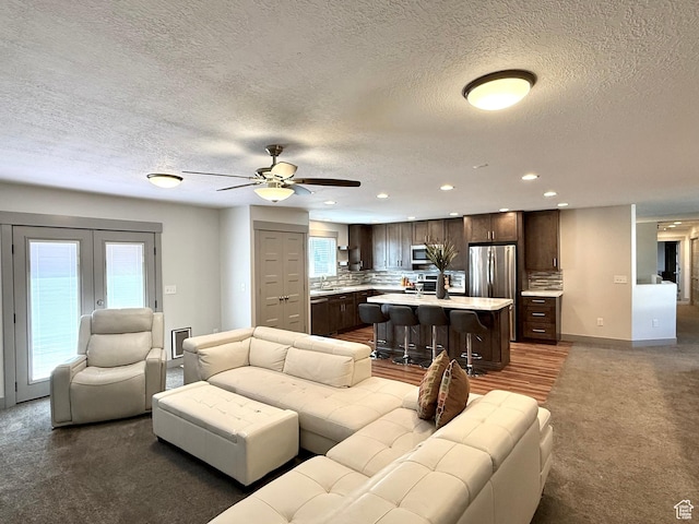carpeted living room featuring a textured ceiling, recessed lighting, a sink, ceiling fan, and french doors