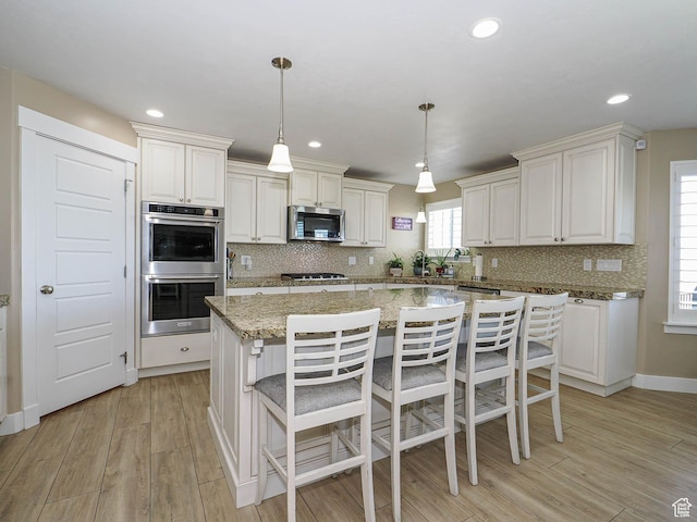 7503 S Bridge Maple Ln, West Jordan, UT 84081 - kitchen with appliances with stainless steel finishes, decorative backsplash, light wood finished floors, a kitchen island, and recessed lighting