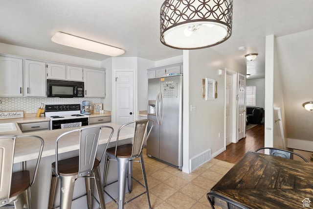 kitchen with stainless steel fridge with ice dispenser, electric range, black microwave, a peninsula, and a kitchen bar
