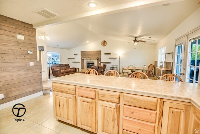 kitchen with light brown cabinets, open floor plan, a brick fireplace, light tile patterned floors, and ceiling fan