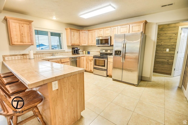 kitchen featuring appliances with stainless steel finishes, light brown cabinetry, a peninsula, a breakfast bar, and a sink