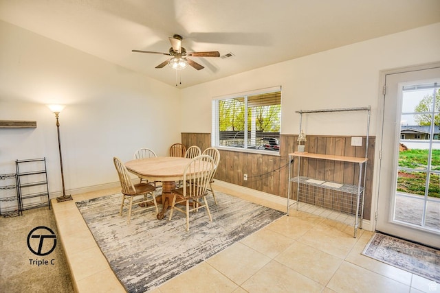 dining room featuring a ceiling fan, healthy amount of natural light, a wainscoted wall, tile patterned floors, and wooden walls