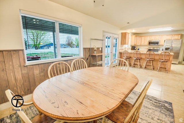 dining area with a wainscoted wall, lofted ceiling, wooden walls, french doors, and light tile patterned floors