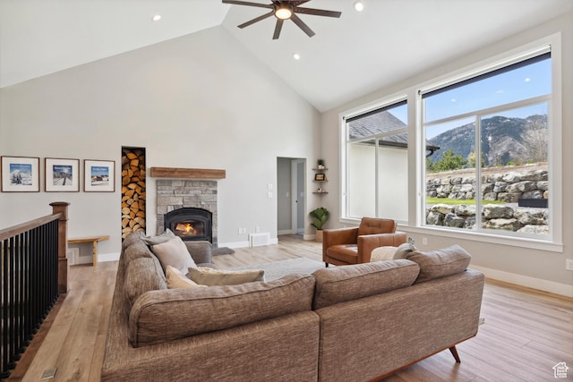 living area featuring a ceiling fan, high vaulted ceiling, light wood-style flooring, a mountain view, and a fireplace