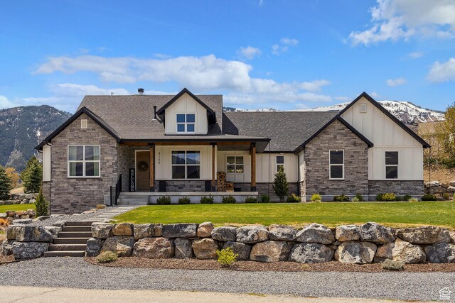 craftsman inspired home with board and batten siding, a mountain view, stone siding, roof with shingles, and a front yard