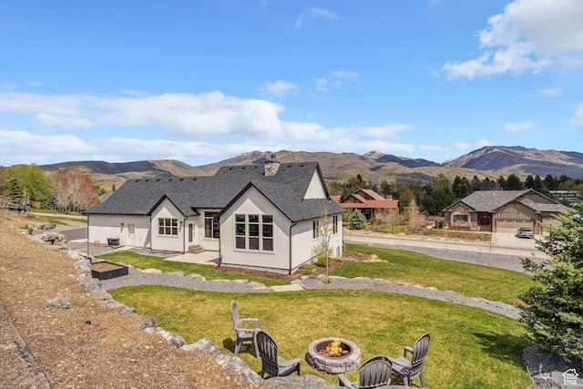 rear view of property featuring an outdoor fire pit, a mountain view, a lawn, and stucco siding