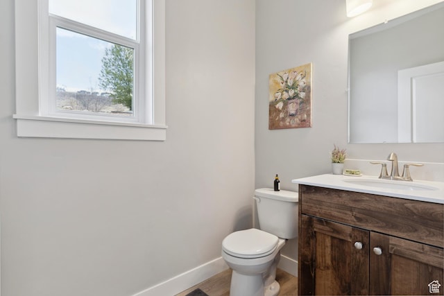 half bath featuring baseboards, toilet, vanity, and wood finished floors
